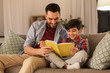 © Syda Productions - family, childhood, fatherhood, leisure and people concept - happy smiling father and little son reading book on sofa at home