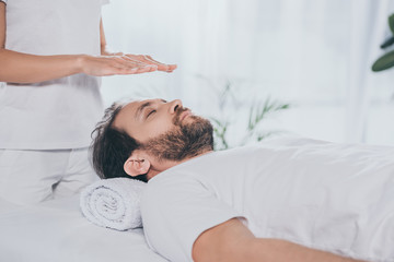 Wall Mural - cropped shot of bearded man with closed eyes receiving reiki treatment above head