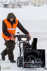 Worker in winter overalls with a snowplow