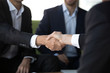 © fizkes - Close up view of two businessmen in suits shake hands at group meeting, business partners handshaking after successful negotiation closing good deal, respect and loyalty, union, reliability concept