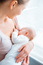 cropped shot of young mother breastfeeding adorable baby at home