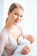 Wall Mural - beautiful young mother breastfeeding baby and smiling at camera