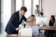 © fizkes - Corporate executive manager consult mature employee help with computer, male mentor manager ceo supervise middle aged female worker teach colleague, office coworkers discuss online project software