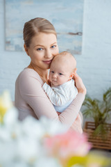 Wall Mural - selective focus of happy young mother hugging infant baby and smiling at camera