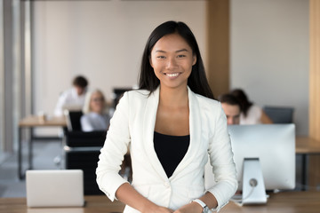 Wall Mural - Smiling young asian business woman looking at camera, happy chinese employee worker, team leader, coach or corporate manager posing in office, millennial korean professional head shot portrait