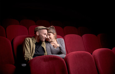 Wall Mural - Young cute couple sitting alone at red movie theatre and having fun