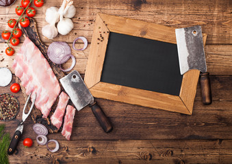 Fresh raw pieces of pork ribs on chopping board and vintage meat hatchet and menu chalk board on wooden background. Fresh tomatoes and red onion with garlic salt and pepper. Space for text