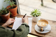Woman Sit At Office Surround With Green Plants, Coffee And Write At Her Note Book