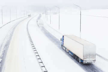 trucks with cargo trailers on the highway in a snow storm. top view of a snowy asphalt road in bad w