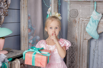 Portrait of cute european little blonde princess girl with crown in beautiful dress in decorated studio in christmas location with toys and christmas tree