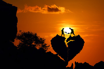 Couple on the broken heart shape rock on the mountain with red sky sunset