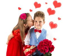Saint Valentine's Day. Pretty Girl With Red Dress Kissing A Gentleman Boy With Blue Vest, Red Butterfly Tie,  Red Roses Bucket And Heart Shaped Gift Box. Valentines Day Kids. Love And Friendship