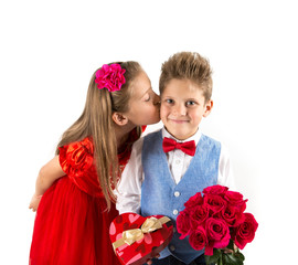 Saint Valentine's day. Pretty girl with red dress kissing a gentleman boy with blue vest, red butterfly tie,  red roses bucket and heart shaped gift box. Valentines day kids. Love and friendship