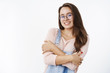 © Cookie Studio - Waist-up shot of cute and kind friendly-looking feminine 20s female in transparent glasses hugging herself with hands crossed over body feeling chilly and smiling at camera over gray background