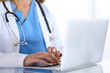 © rogerphoto - Doctor typing on laptop computer while sitting at the glass desk in hospital office. Physician at work. Medicine and healthcare concept
