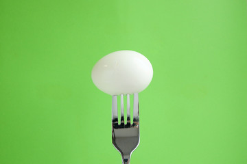 Wall Mural - Boiled egg on a green background. Food on fork