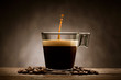 Black coffee in glass cup with coffee beans and jumping drop, on wooden table