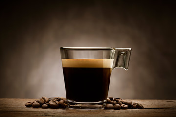 Black coffee in glass cup with coffee beans on wooden table