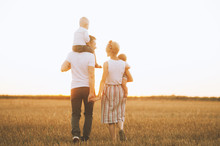 Happy Young  Family Is Walking Along The Wheat Field At Sunset. The Concept Of Family And Love
