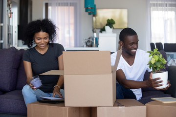 Wall Mural - African american happy couple unpacking cardboard boxes in living room moving into new home, young black family packing stuff preparing for relocation or renovation in house or flat, removals concept