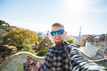 Wall Mural - Travel and holidays concept - Handsome man looking at camera taking photo with smart phone smiling in Park Guell, Barcelona, Spain.