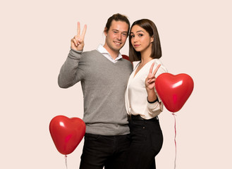 Couple in valentine day smiling and showing victory sign with both hands over isolated background