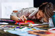 Young woman artist is falling asleep while draw sketch in her workshop. Closeup of creative workplace on wooden table with drawing tools, pencils, pastels, tubes, watercolors. Art concept.