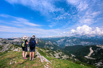 rear view of man and woman in middle age with backpack hiking in beautiful mountain panorama, sloven