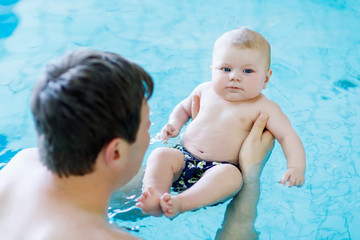 Wall Mural - Happy middle-aged father swimming with cute adorable baby in swimming pool. Smiling dad and little child, newborn girl having fun together. Active family spending leisure and time in spa hotel