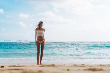 Beautiful tanned girl standing on beach with white sand and blue ocean