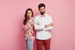 Photo of unhappy sullen couple have dispute and misunderstanding, not speak to each other after quarrel, stand back, keep arms folded, isolated over pink background. People and conflict concept