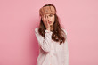 Upset tired young woman has not enough sleep, touches face with hand, wears eyemask and casual jumper, isolated over pink background, slept bad at night. People, tiredness and awakening concept