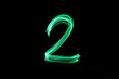 Long exposure, light painting photography.  Single number two in a vibrant neon green colour against a black background