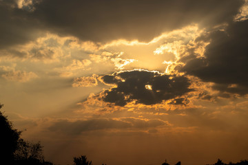 Gray cloud floating come to cover sun causing an orange beam go around sky some clouds change color from white to orange and gold.