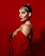 Beautiful attractive girl with smooth hair and in a red fur coat made of faux fur posing in the studio on a red background.	