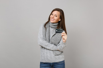 Wall Mural - Stunning young woman in gray sweater, scarf holding credit bank card isolated on grey background in studio. Healthy fashion lifestyle people sincere emotions, cold season concept. Mock up copy space.