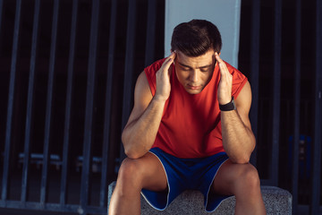 Unhappy young male athlete having headache outside