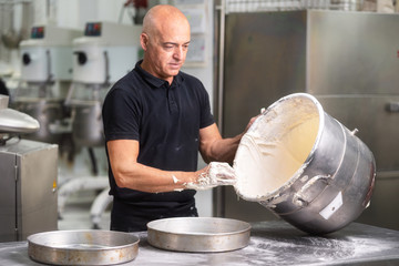 Wall Mural - Professional pastry Chef whisking cream in big casserole at pastry shop kitchen .