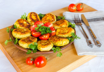 Homemade ruddy cheese and potato cutlets, decorated with fresh tomatoes and parsley, in ceramic plate on wooden board