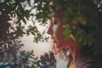 Portrait of a beautiful young woman with dark hair in a frame of branches and green leaves, summer and spring sensual portrait, natural beauty