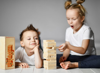 two kids boy and girl in white t-shirts are on the floor and play jenga