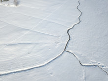 Aerial view of snow covered plain with brook flowing in straight line through landscape.