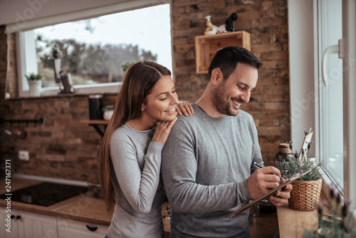 Portrait of a cute millennial spouses writing a list at modern cozy apartment Tableau sur Toile