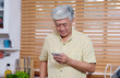 © mangpor2004 - Senior asian man using smart phone while standing in kitchen at home, people and technology