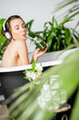 © rh2010 - Young relaxed woman listening to the music and drinking smoothie while lying in the retro bathtub at the beautiful bathroom with green plants