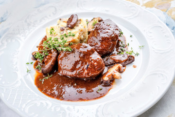 Wall Mural - Traditional German braised pork cheeks in brown red wine sauce with mushroom and mashed potatoes as closeup on a classic design white plate