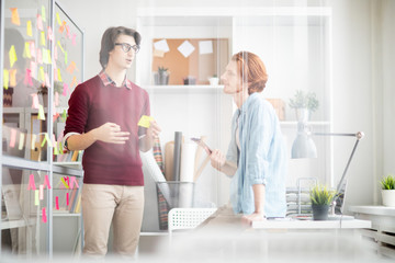 Poster - Two young managers in casualwear discussing working or organization moments at meeting in office