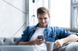 © opolja - Young man using his smartphone for online banking - sitting on sofa with laptop on leap.