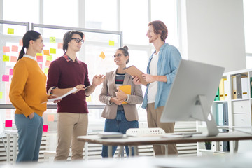 Poster - Group of four young casual colleagues brainstorming and discussing their ideas for new design project in office