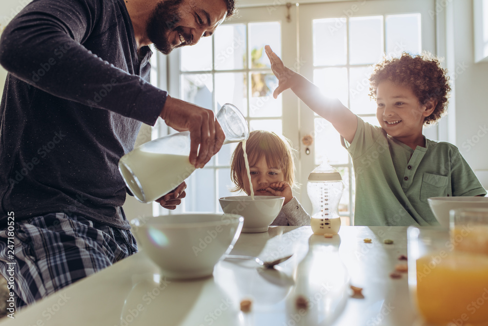 Smiling father pouring milk in to bowls for breakfast - obrazy, fototapety, plakaty 